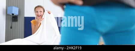 Frau, die auf dem Bett sitzt, sieht den Mann in kurzen Hosen aus der Nähe an Stockfoto