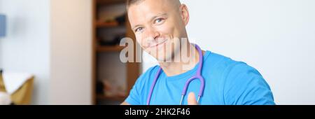 Porträt eines jungen lächelnden männlichen Arztes, der die Daumen hoch hält Stockfoto