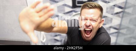 Ein junger Mann schreit, während er in der Nähe auf der Toilette sitzt Stockfoto