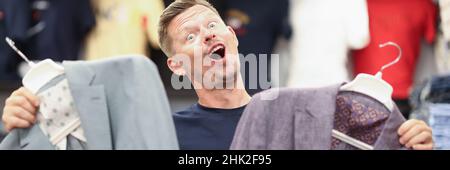 Porträt eines glücklichen Mannes, der zwei Jacken im Laden hält Stockfoto
