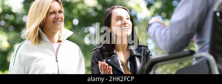 Zwei junge Frauen kommunizieren mit einem Mann im Rollstuhl im Park Stockfoto