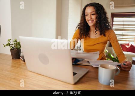 Afroamerikanische Geschäftsfrau, die von zu Hause aus geschäftlich mit Kunden auf einem Laptop zusammenarbeitet Stockfoto