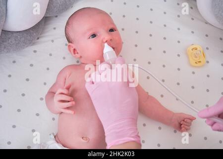 Der Arzt entfernt bei einem Neugeborenen eine laufende Nase mit einer Absaugvorrichtung. Krankenschwester in Uniform behandelt Kindernase für Grippe Stockfoto