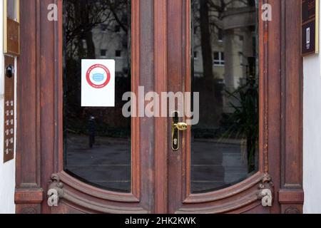 Berlin, Deutschland. 01st. Februar 2022. Hinter der Glasscheibe der Eingangstür zu einem Wohnhaus am Viktoria-Luise-Platz im Berliner Stadtteil Tempelhof-Schöneberg hängt ein Schild mit dem Aufschrift "Please only wear a mouth guard". Quelle: Soeren Stache/dpa-Zentralbild/dpa/Alamy Live News Stockfoto