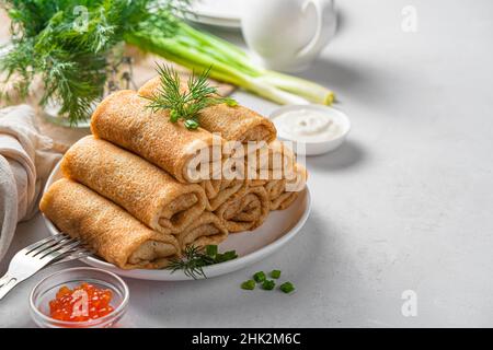 Gefüllte Pfannkuchen mit frischen Kräutern, rotem Kaviar und saurer Creme auf hellem Hintergrund. Seitenansicht, Kopierbereich. Traditionelle russische Pfannkuchen. Pfannkuchentag. Stockfoto