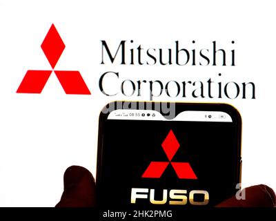 In dieser Abbildung wird das Logo der Mitsubishi Fuso Truck and Bus Corporation auf einem Smartphone-Bildschirm mit einem Mitsubishi Corporation-Logo im Hintergrund angezeigt. Stockfoto