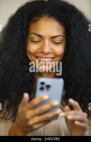 Glückliche schwarze Frau, die online mit Smartphone-App kauft. Fröhliche afrikanische Frau, die im Internetgeschäft mit toothy Lächeln einkaufen. Person, die Geld verdient Stockfoto