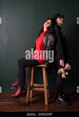 Zwei Teenager-Mädchen im Grunge-Stil, gegen eine dunkelgrüne Wand gekleidet. Ein weiches Spielzeug in den Händen eines der Mädchen. Stockfoto