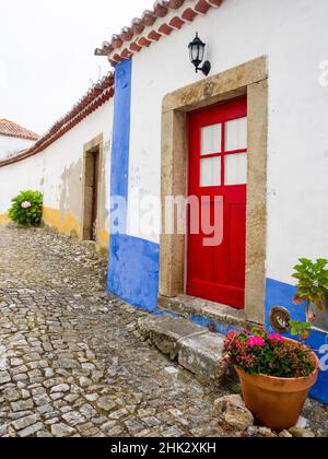 Portugal, Obidos. Leuchtend rote Tür entlang des Gehwegs in der historischen ummauerten Stadt Obidos. Stockfoto