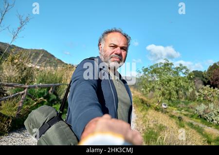 Folge mir. Der Mann hält und zieht die Hand des Fotografen, während er auf einer ländlichen Straße geht. Konzept der Vereinigung und des neuen modernen Lebens im Einklang mit der Natur. Stockfoto