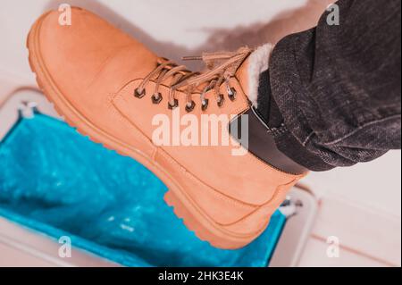 Gerät für die automatische Verkleidung von Stiefelabdeckungen, ein Mann in braunen Schuhen legt Stiefelabdeckungen, mechanische clintoper an. Stockfoto