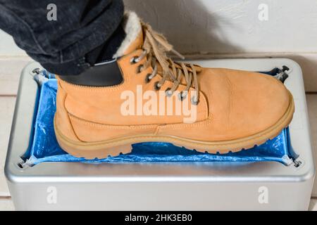 Gerät für die automatische Verkleidung von Stiefelabdeckungen, ein Mann in braunen Schuhen legt Stiefelabdeckungen, mechanische clintoper an. Stockfoto