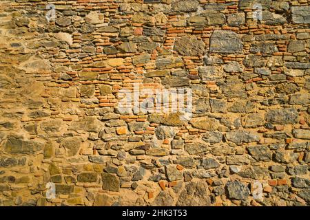 Ziegel- und Steinmauer in warmen Tönen einer alten mittelalterlichen Mauer. Konzept mit stark texturierten Hintergründen. Stockfoto