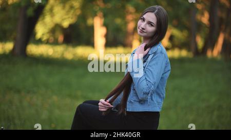 Ein junges Mädchen streichelt ihr langes Haar, während es im Park sitzt. Stockfoto