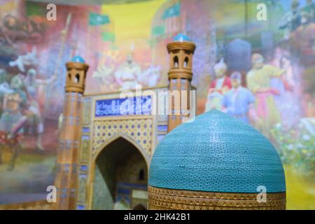 Ein Detail eines Modells der Bibi-Khanym-Moschee aus Samarkand und ein großes Wandbild, das Führer der Seidenstraße im Hintergrund zeigt. Im Staatsmuseum Stockfoto