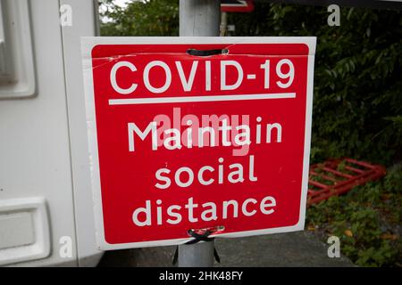 Red covid-19 unterhält soziales Fernschild am fährhafen von windermere in Far sawrey mit Blick auf bowness-on-windermere Lake District, cumbria, Stockfoto