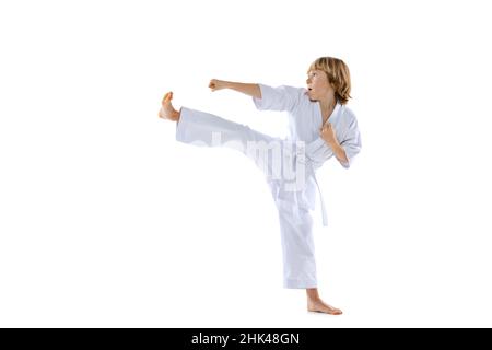 Ein sportlicher kleiner Junge, Taekwondo-Athleten, die Doboks tragen und alleine auf weißem Hintergrund üben. Konzept des Sports, Kampfkunst Stockfoto