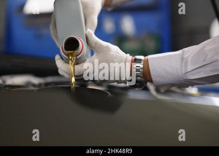 Meister der Werkstatt gießt Motoröl unter die Motorhaube des Autos aus der Nähe Stockfoto