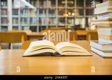 Alte Lehrbücher sind offen und stapeln Bücher auf einem Holztisch auf einem unscharfen Bücherregal im Hintergrund des Bibliotheksraums Stockfoto