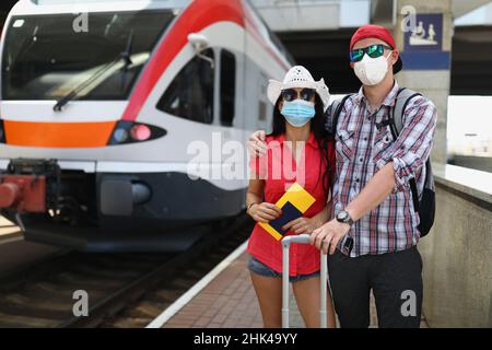 Junges Paar in schützenden medizinischen Masken, das in der Nähe des Zuges mit Fahrscheinen in den Händen steht Stockfoto