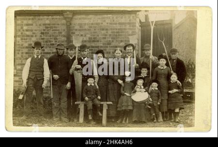 Wunderbare viktorianische Carte de Vistie (CDV) oder Visitenkarte von Gruppenarbeitern und ihren Familien - Frauen und Kinder, mehrere Charaktere auf viktorianischer Farm. Alle sind in dem gekleidet, was ihr einziges Kleidungsstück gewesen wäre - ihre sonntäglichen besten. Die Männer tragen Bowler-Hüte, um ihre Köpfe zu schützen. Für das Foto mit den Werkzeugen ihres Fachs posieren: Wartungsteam mit Holzbearbeitungswerkzeugen, Spaten und einer Pistole und Bauernhände mit ihren landwirtschaftlichen Werkzeugen - Pitinerant Gabel, Spaten und Rechen, von dem Wanderfotografen A. (Alfred) Arnell aus Scarborough, Yorkshire, England, um 1880er Jahre Stockfoto