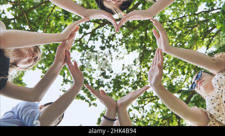Eine Gruppe von Mädchen macht aus ihren Händen eine Herzform vor dem Hintergrund von Ästen. Stockfoto