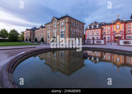 Burg Bruchsal zur blauen Stunde mit einem Brunnen im Vordergrund und Spiegelung im Wasser. Stockfoto