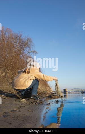 Junge Frau, die den Müll aus einem Fluss in der Stadt aufsammelt Stockfoto