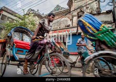 Rikscha-Abzieher auf den Straßen von Puran Dhaka - Old Dhaka in Bangladesch. Die Rikschas sind pedalbetriebene Dreiräder, wurden aber früher von Hand gezogen, daher 'Rikschas-Abzieher'. Heutzutage werden viele der Rikschas sogar auf Elektromotor umgerüstet. Stockfoto