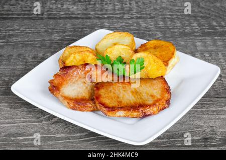 Teller mit gebratenen Fleischstücken, goldenen pommes frites und Petersilienblättern auf altem Holzhintergrund. Selektiver Fokus Stockfoto