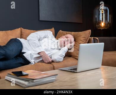 Müde, reifer Geschäftsmann, der im Büro oder zu Hause auf der Couch schläft. Konzept für Überstunden oder Überlastung bei der Arbeit. Hochwertige Fotos Stockfoto