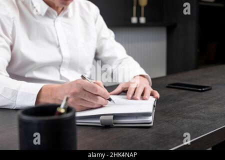 Geschäftsmann nimmt sich Notizen oder schreibt im Planer am Büroarbeitsplatz eine Agenda. Geschäftsplanung und Strategiekonzept. Hochwertige Fotos Stockfoto