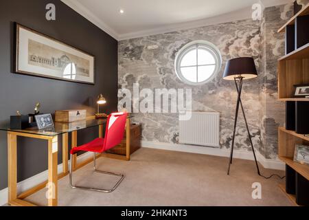 Alconbury Weald, Cambridgeshire - Oktober 17 2016: Arbeitszimmer mit Schreibtisch aus Glas und rotem Stuhl in stilvollem, modernem Zuhause Stockfoto
