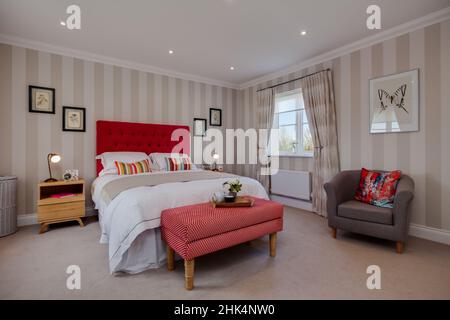 Alconbury Weald, Cambridgeshire - Oktober 17 2016: Modernes, stilvolles Schlafzimmer in Aspiration Chic Home mit auffallend rotem Kopfteil und modischem Fell Stockfoto