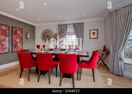 Alconbury Weald, Cambridgeshire - Oktober 17 2016: Beeindruckendes Esszimmer im modernen Luxushaus mit Tischstühlen, die mit hellrotem Stoff bezogen sind Stockfoto