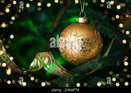 Nahaufnahme der goldenen Kugel auf dem weihnachtsbaum. Weihnachtstanne mit Dekoration auf dunklem Hintergrund mit Bokeh-Lichtern. Weihnachtsschmuck am Weihnachtsfeiertage Stockfoto