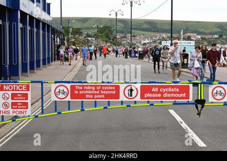 Swanage, Dorset, England - Juni 2021: Metallbarriere über die Promenade an der Strandpromenade der Stadt, mit Warnhinweisen für Radfahrer zum Absteigen Stockfoto