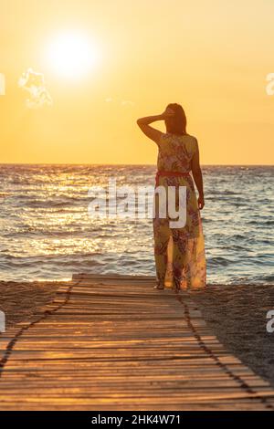 Charmante Frau, die das Meer bei Sonnenuntergang betrachtet und am Strand von Matala, Kreta, den griechischen Inseln, Griechenland, Europa steht Stockfoto