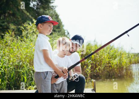 Ein Vater mit zwei jungen Söhnen fischt im Sommer am Wochenende am See Stockfoto