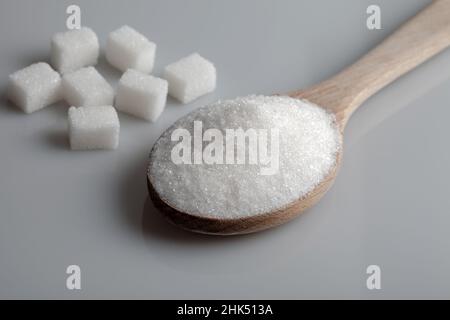 Granulatzucker und Zuckerwürfel in Holzlöffel auf grauem Hintergrund Stockfoto