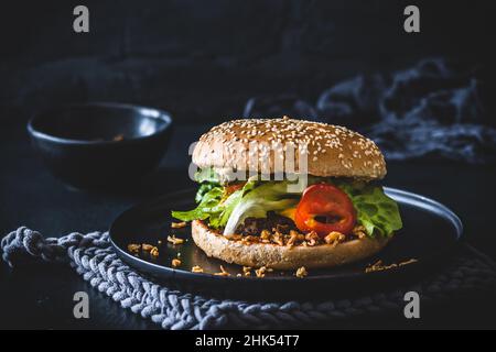 Hausgemachter Käse-Burger mit gerösteten Zwiebeln auf schwarzem Teller und schwarzem Hintergrund Stockfoto