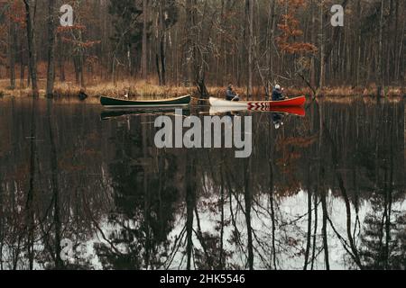 Kanu paddeln Lifestyle: Zwei Personen in einem Boot schleppen ein leeres Schiff in den Waldsee. Wunderschöne Herbstlandschaft mit Menschen paddeln kanadische Ca Stockfoto