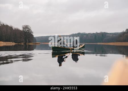 Zwei Männer paddeln in einem kanadischen Kanu auf dem See. Aktiver Lebensstil, ein Holzboot auf der Oberfläche eines ruhigen Waldsees im Frühling oder Herbst Stockfoto