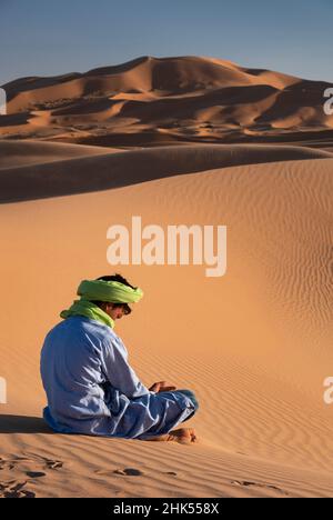 Ein Berbermann in traditioneller Kleidung sitzt zwischen den Sanddünen von Erg Chebbi, Sahara-Wüste, Marokko, Nordafrika, Afrika Stockfoto