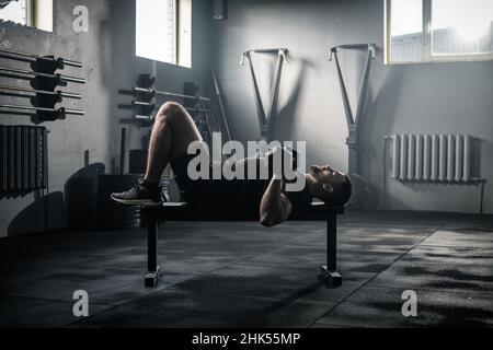 Sportlicher Mann hat Arme Workout in dunklen Turnhalle. Stockfoto