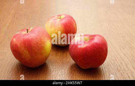 Drei große, leuchtend rote Äpfel auf dem Tisch liegen auf einem Holztisch. Nahaufnahme im Innenbereich Stockfoto