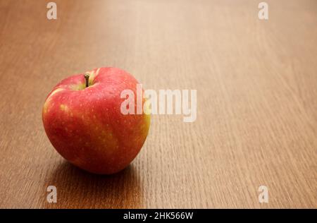 Großer leuchtend roter Apfel auf dem Tisch auf Holztisch. Nahaufnahme im Innenbereich Stockfoto