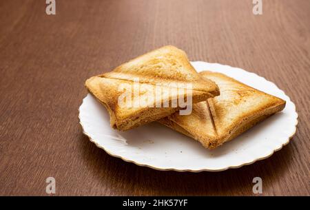 Zwei geröstete, ruddige und appetitliche Brotscheiben auf einem weißen Teller. Nahaufnahme im Innenbereich Stockfoto