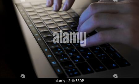 Nahaufnahme der Hände des Mannes, die auf der Tastatur tippen. Konzept. Herrenhände geben nachts Text auf der Tastatur ein. Stockfoto