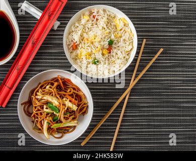 Nudeln mit Gemüse und Reispilaf mit Ei und Mais in einer weißen Schüssel auf dunklem Grund Stockfoto